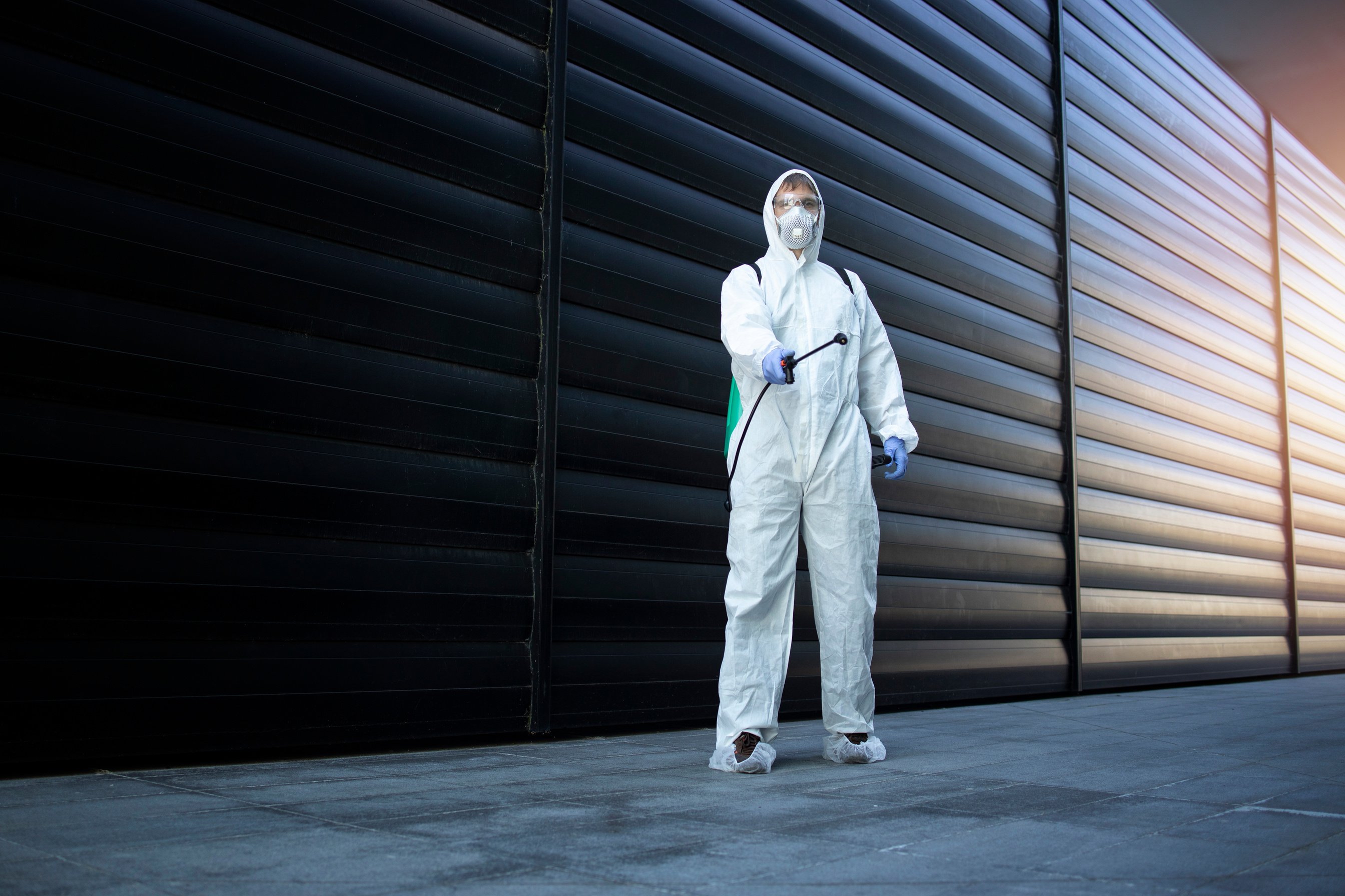 Shot of exterminator person in white chemical protection suit doing disinfection and pest control and spraying poison to kill insects and rodents. Successful pest control and extermination.